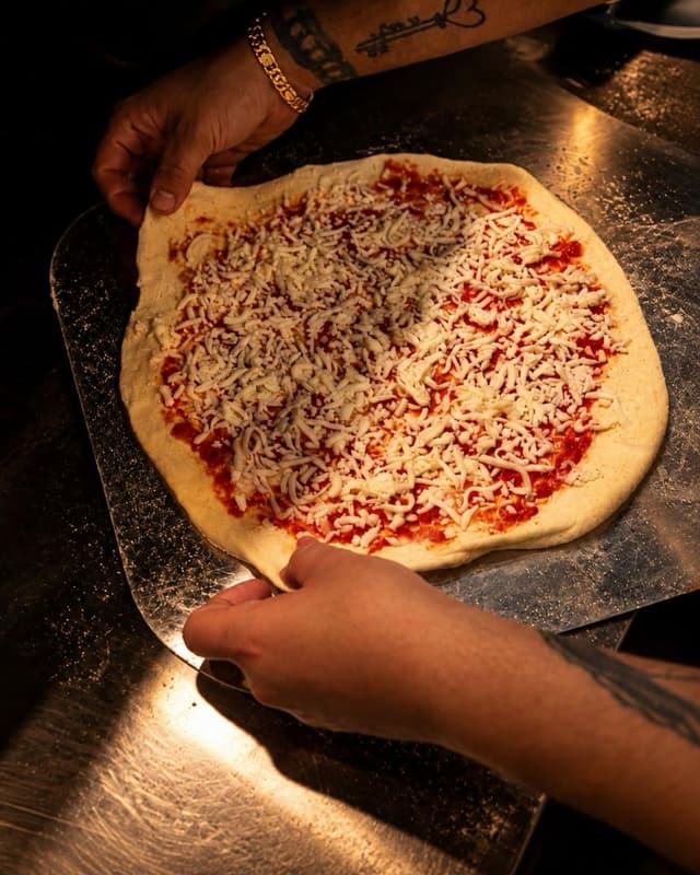 A pizza base stretched and topped by hand on a steel counter at The Goodfellas Pizzeria.